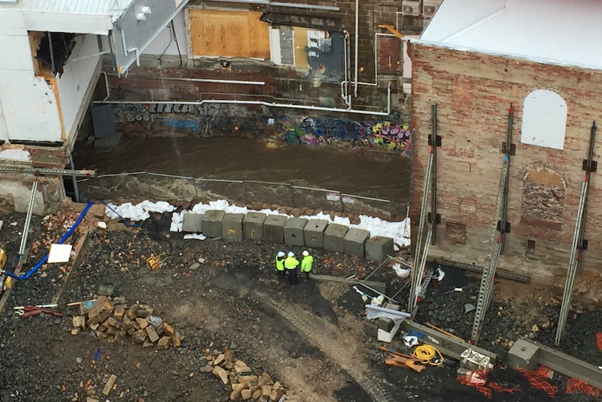 Workers survey the rivulet under the Myer building site, in Hobart.