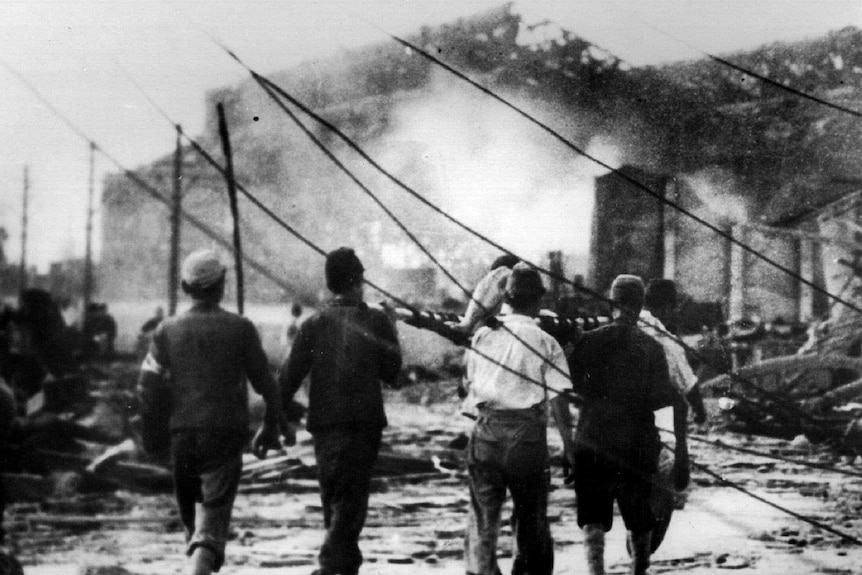 Japanese air raid workers carry a victim of the atomic bomb in Hiroshima away from smoking ruins