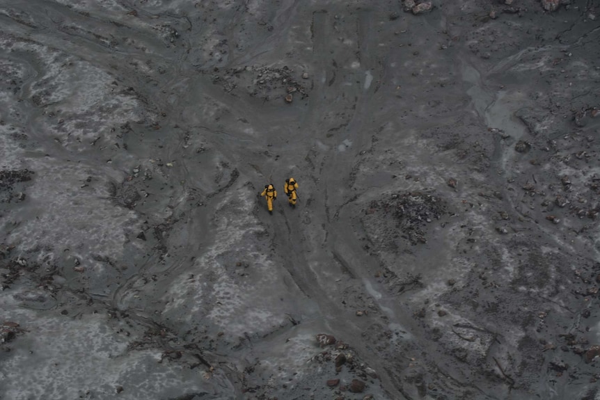 An aerial image of two people in yellow suits walking on a barren landscape