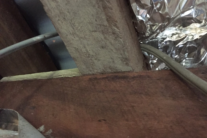 a wire running over a wooden plank and under metallic insulation material