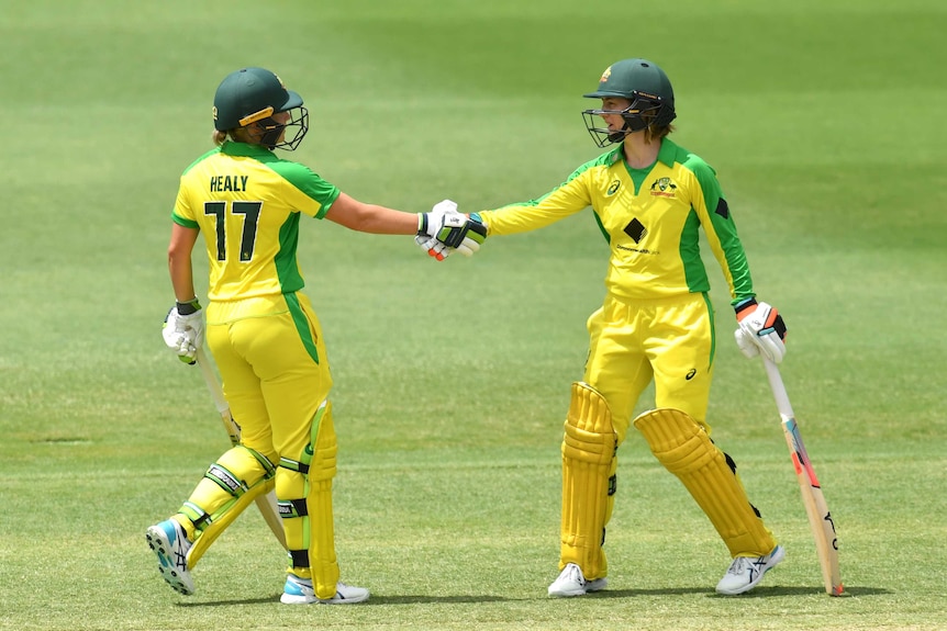 Two Australian female cricketers shake hands while batting against New Zealand in Brisbane.