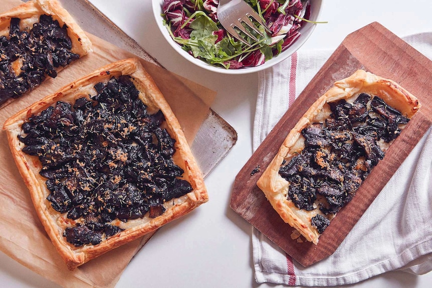 One and half mushroom tarts sitting on a baking tray, a greens and radicchio salad, and half tart on a chopping board, for lunch