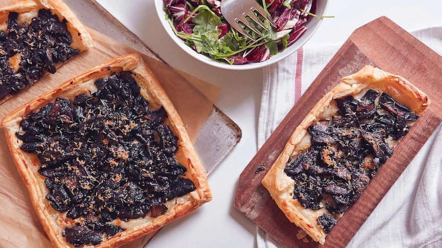 One and half mushroom tarts sitting on a baking tray, a greens and radicchio salad, and half tart on a chopping board, for lunch