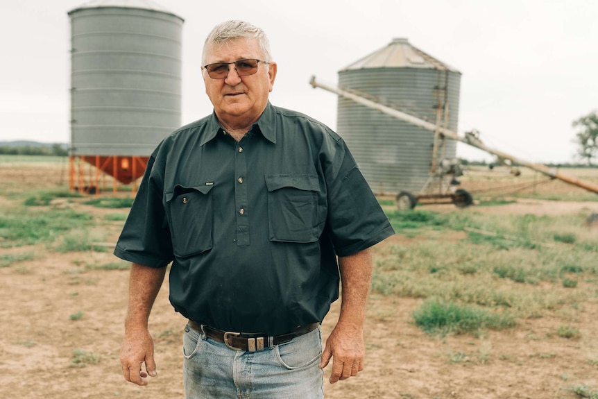 A man with a green shirt and glasses looking at camera with grain silos in background