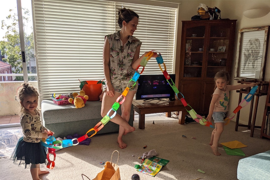 Ed Coper's wife and two daughters hold up a coloured crepe paper chain in a living room
