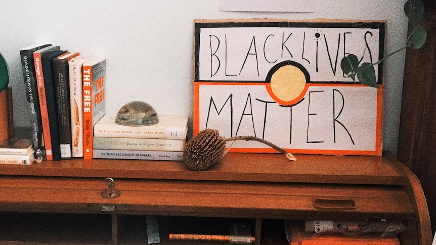 A desk with books stacked on the left and a hand-drawn poster with the words Black Lives Matter written on it