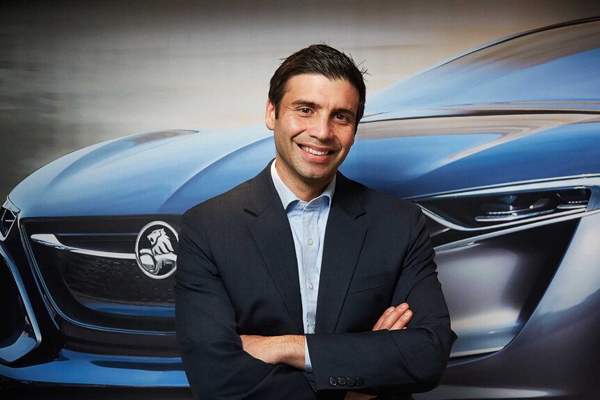 Holden interim managing director Kristian Aquilina poses in front of a photo of a Holden sports car.