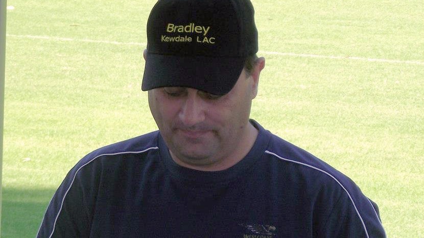 Bradley Robert Edwards stands looking at a card outdoors wearing a blue shirt and black hat bearing the name Bradley on it.