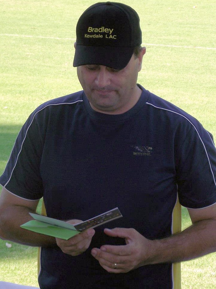 Bradley Robert Edwards stands looking at a card outdoors wearing a blue shirt and black hat bearing the name Bradley on it.