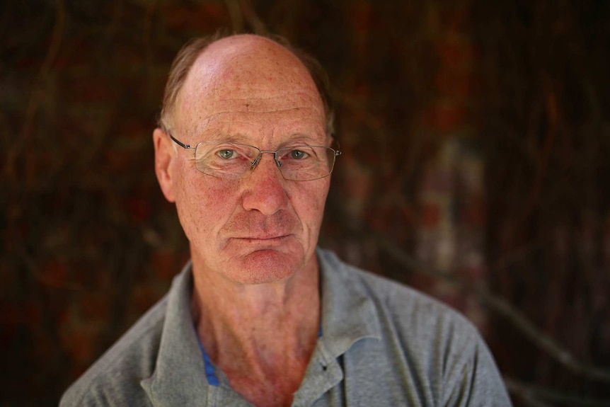 A portrait of a balding man wearing glasses and a grey polo shirt.