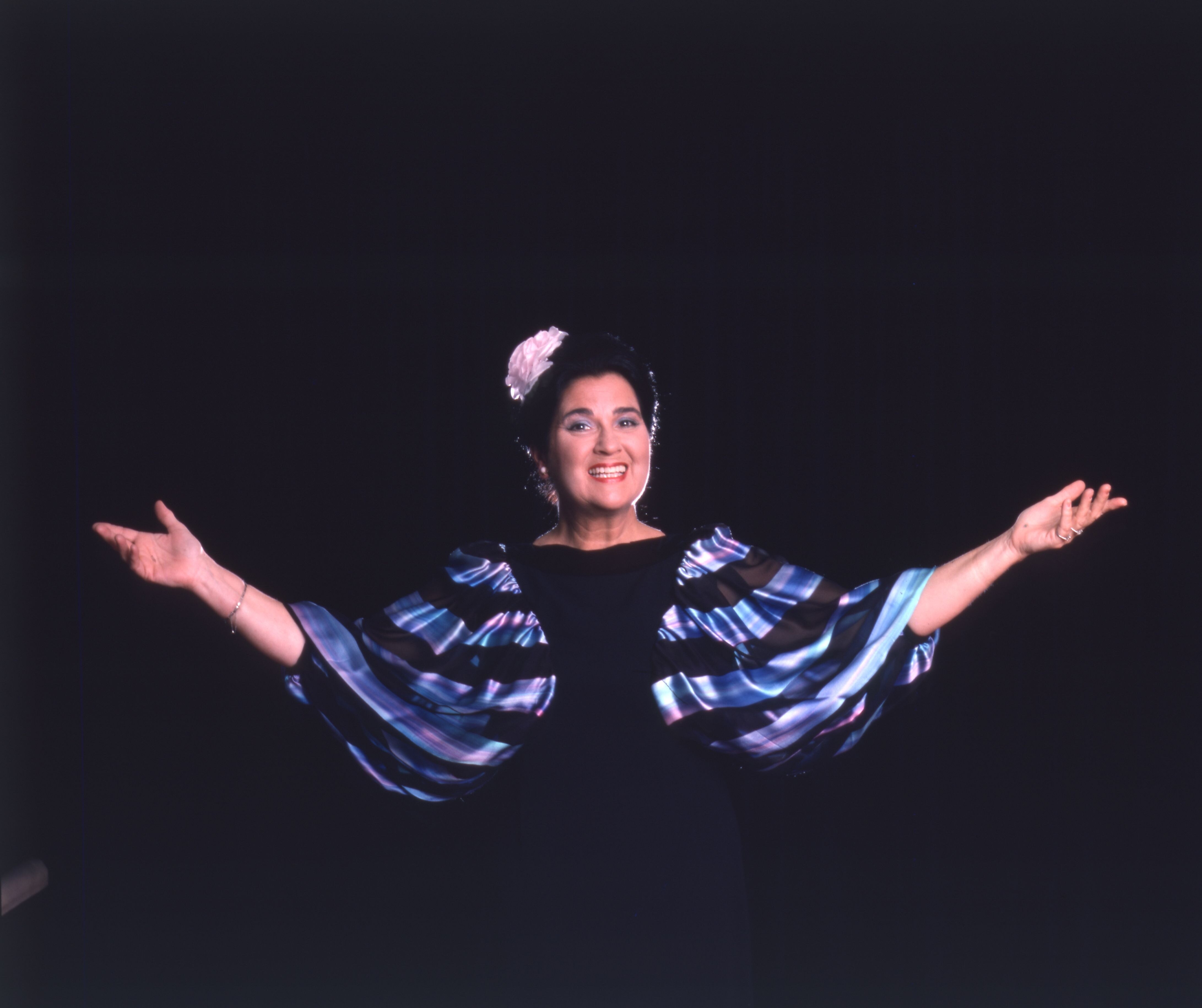 Soprano Elly Ameling stands with arms outstretched against a black background