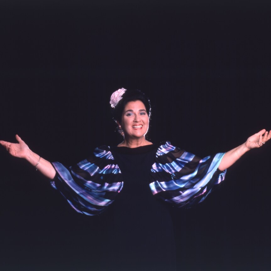 Soprano Elly Ameling stands with arms outstretched against a black background