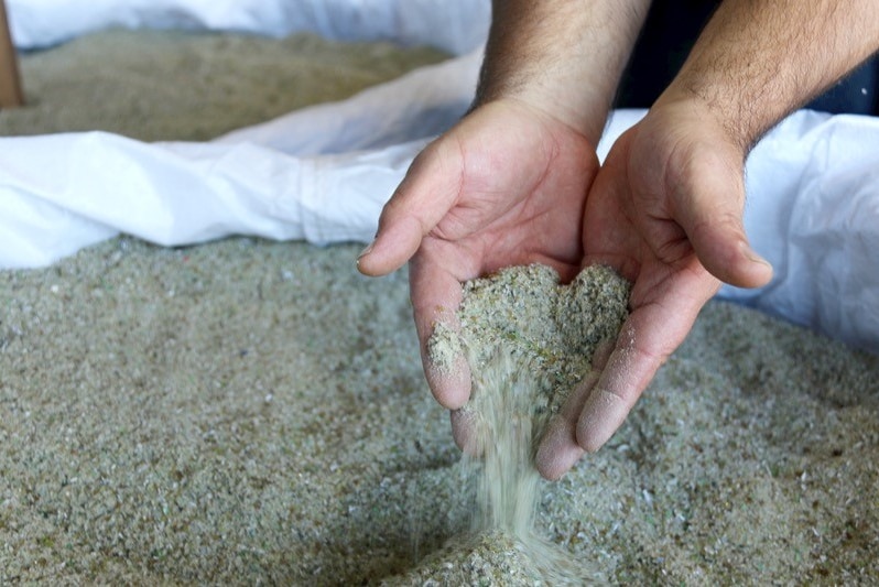 A close up of grains of sand made from recycled glass being poured through a pair of hands.