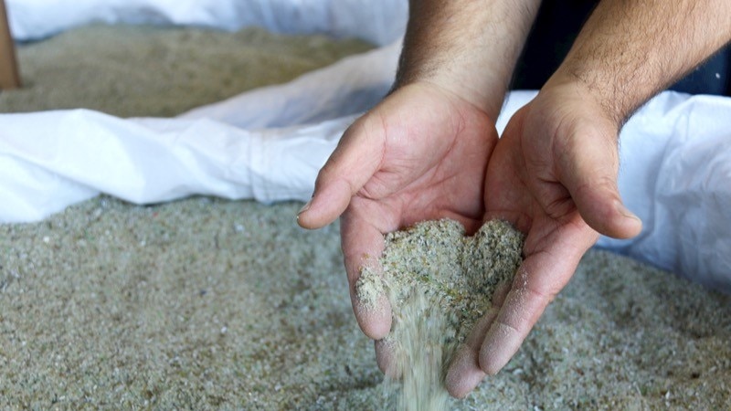 A close up of grains of sand made from recycled glass being poured through a pair of hands.