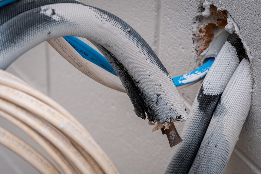 a white tube with copper wiring inside hangs out of a hole in a brick wall