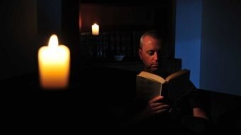 A man reads a book by candlelight.