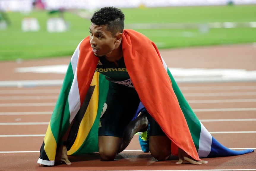 Wayde van Niekerk knelling on the track with the South African flag draped around him.
