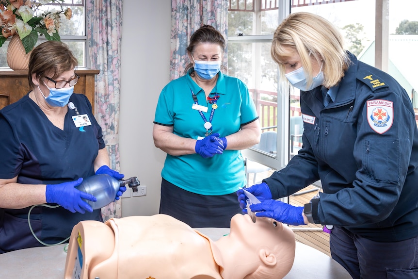 Three women stand around a dummy