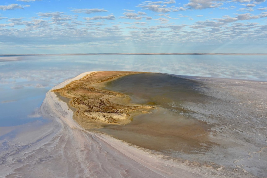 A island in the middle of water. There is a white salt spit coming out of the side