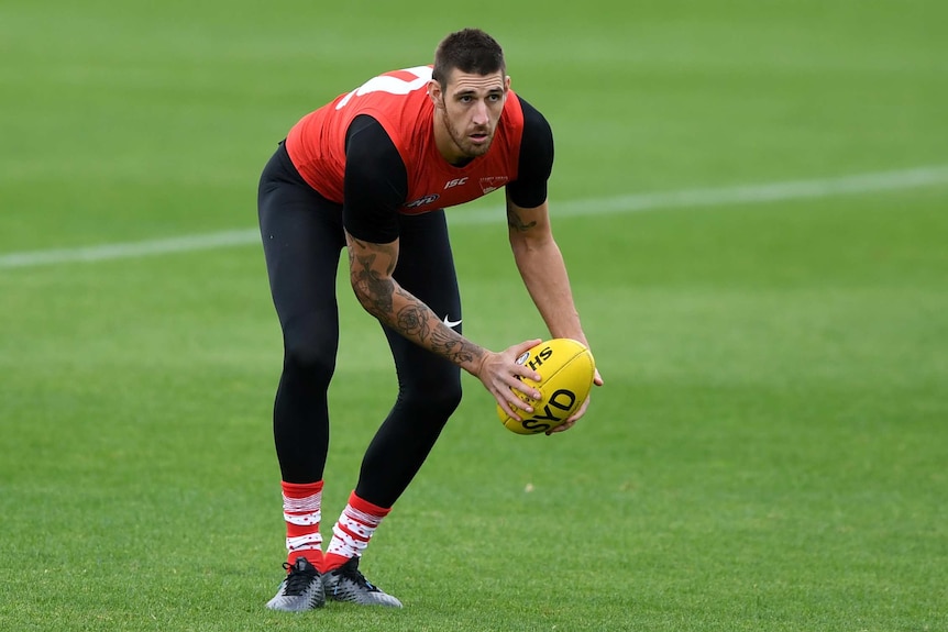 A Sydney Swans AFL player bends over as he holds the ball in both hands at a training session.