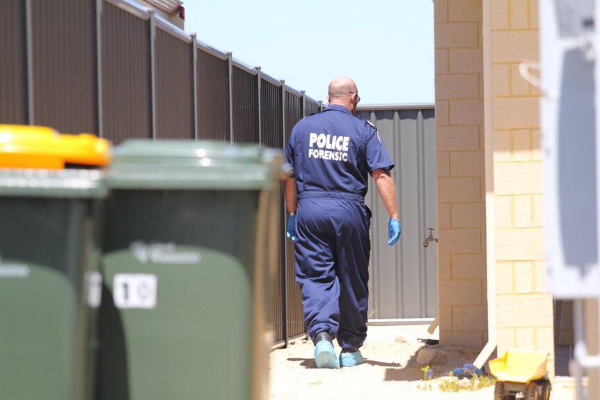 A forensics officer walks down the side of a home.