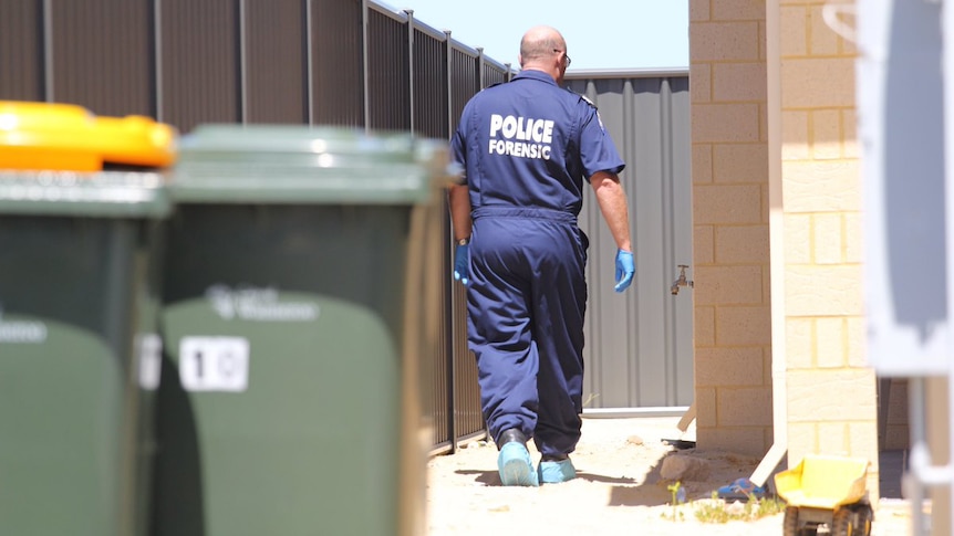 A forensics officer walks down the side of a home.