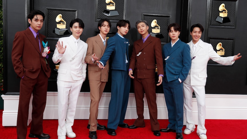 The seven members of bts pose on the grammys red carpet wearing different coloured suits