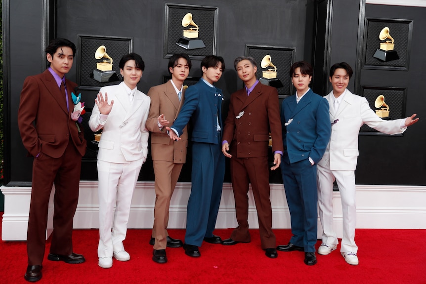 The seven members of bts pose on the grammys red carpet wearing different coloured suits