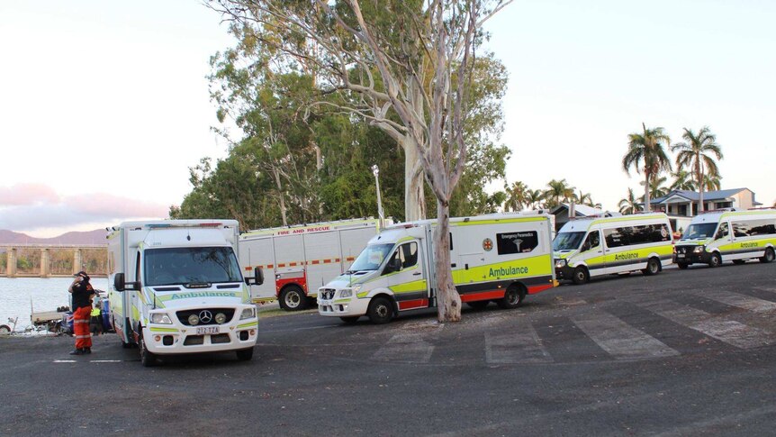 a line of ambulances and fire trucks waits next to the Fitzroy River surrounded by gum trees