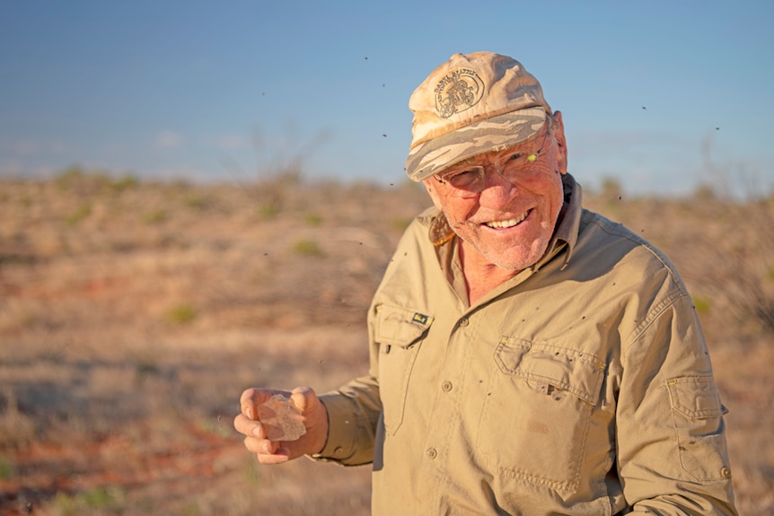 smiling man holds old photographic glass plate up to show camera.  He's standing in the Simpson desert with blue skies