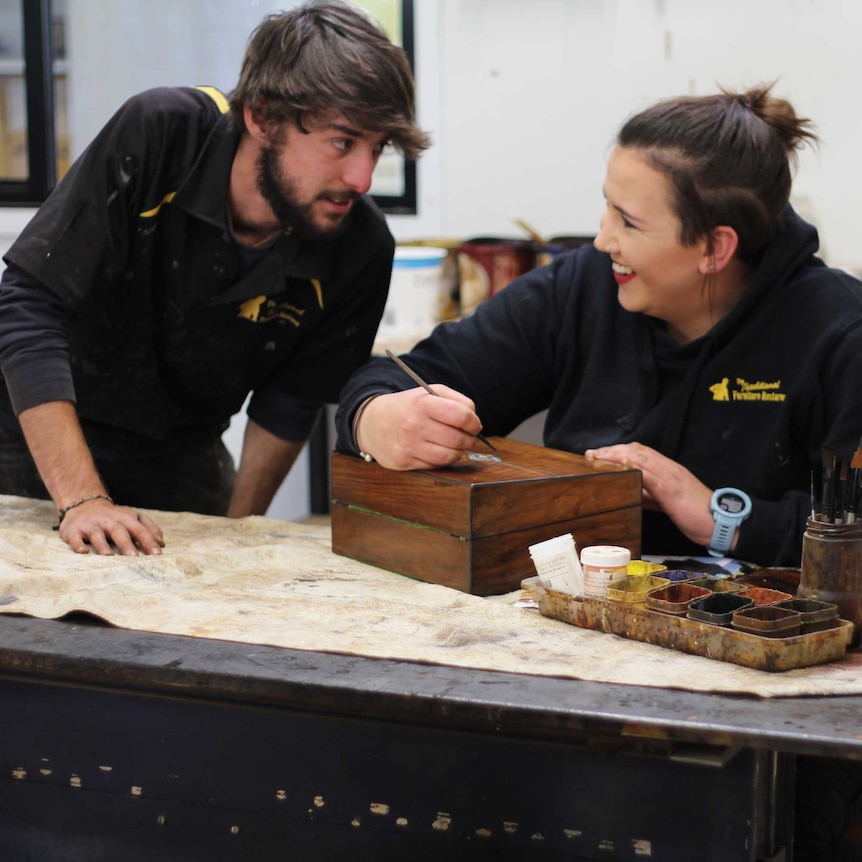 Two people helping to restore an damaged wooden box at The Traditional Furniture Restorer in Queanbeyan.