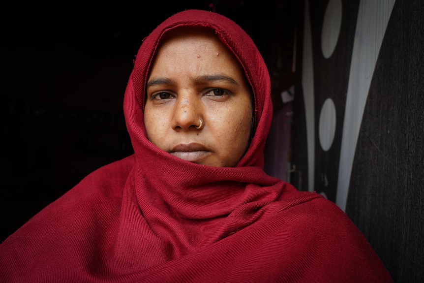 A woman wearing a red-maroon headscarf looks straight down the barrel