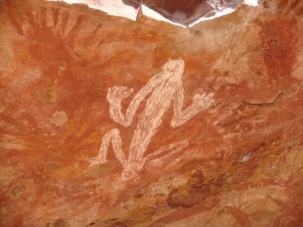 An Indigenous rock painting, featuring white ochre on a red-tinged background.