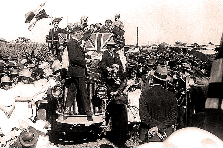 Black and white photo of a parade led by a steam engine on a float in the main street of Ballina.
