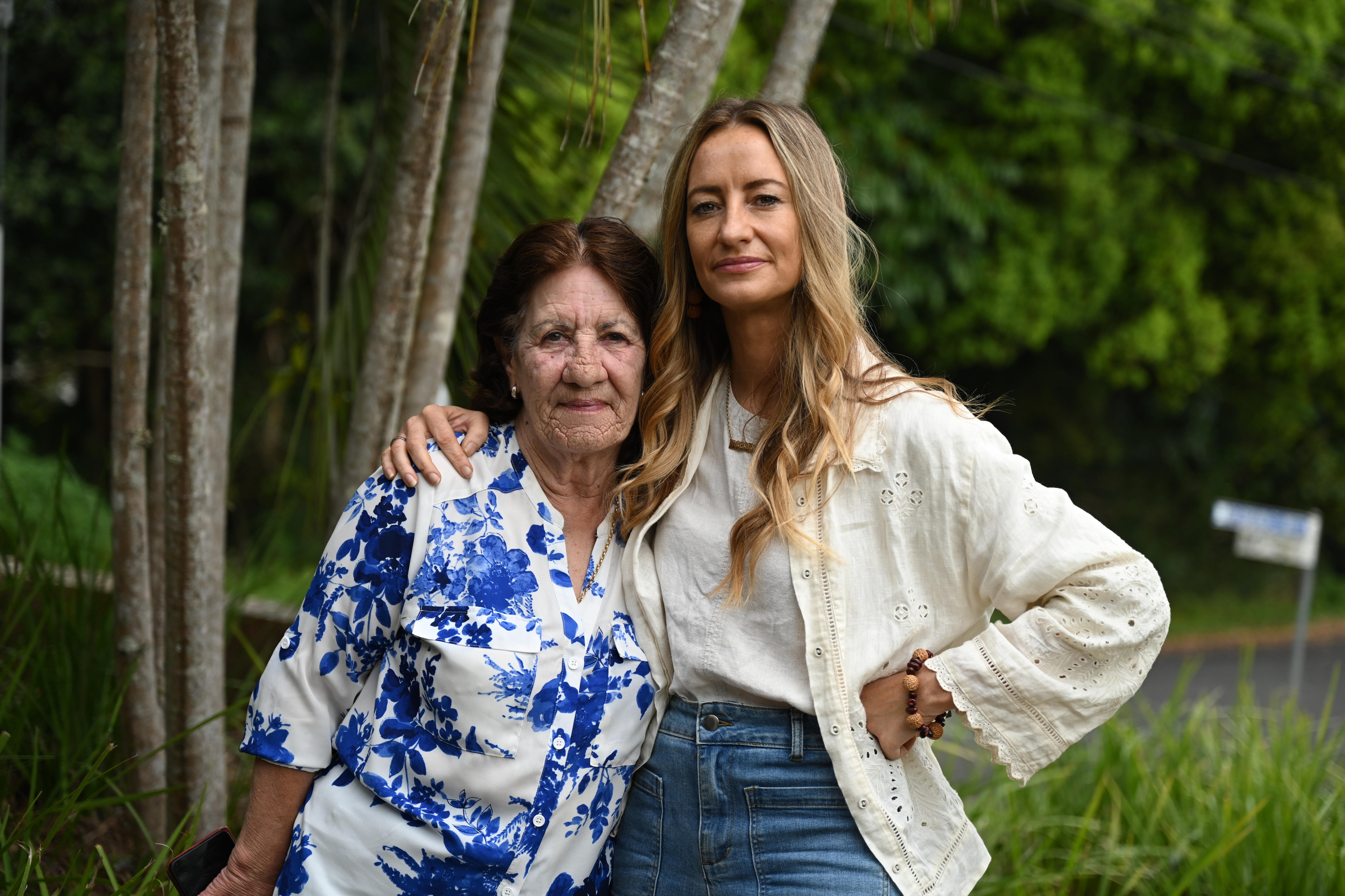 Two women standing with arms around each other in front of trees.