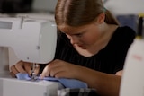 A young girl in a black top sewing a blue piece of fabric on a machine