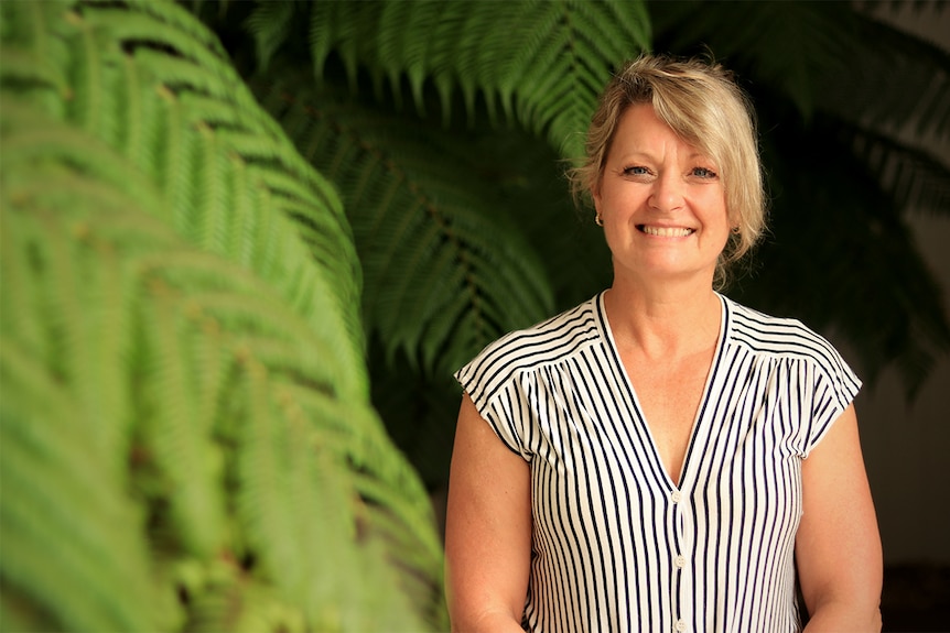 Karen Dempster smiles at the camera while standing near some indoor ferns.