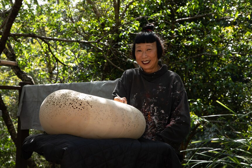 Lindy Lee at work on a sculpture in her garden, smiling.