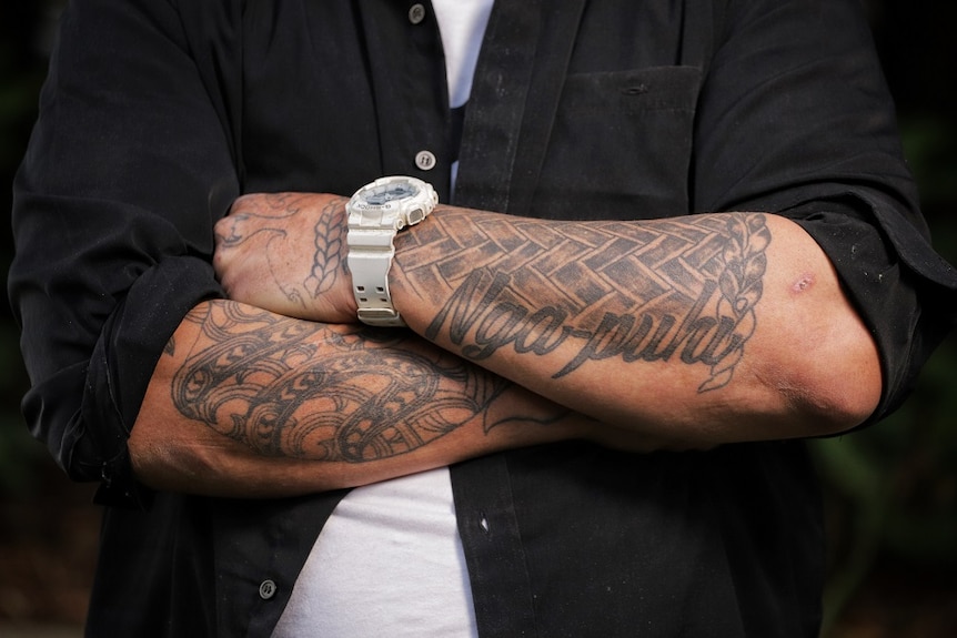 A man's heavily tattooed arms folded across his chest.