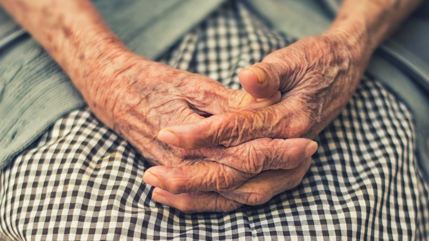 A pair of wrinkled hands folded in a lap.