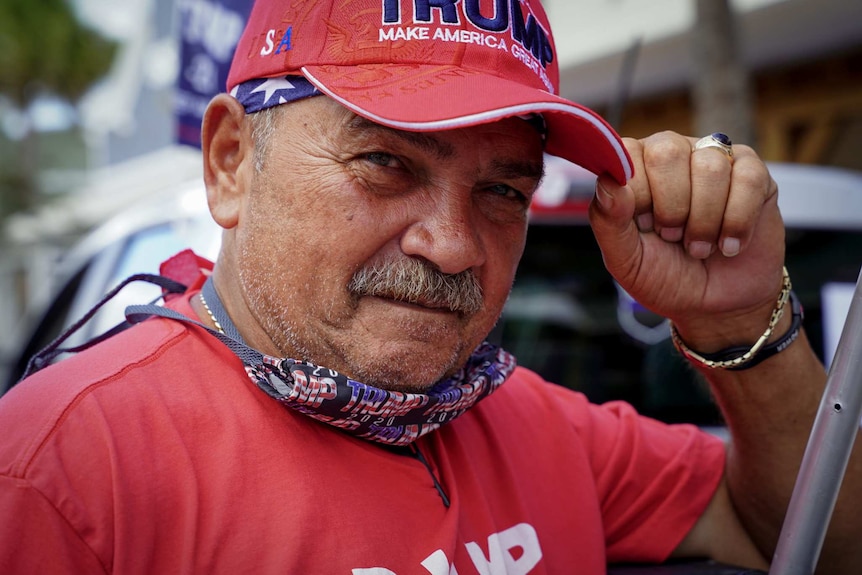 A man grab his hat with Trump make america great again written on it stares at the camera