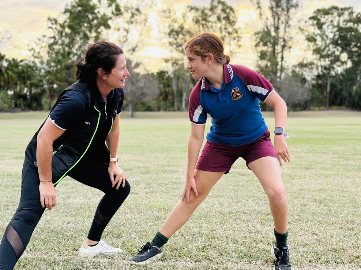 A woman and girl stretching on a patch of grass while looking at each other