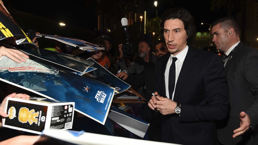 A man in a suit signs posters brandished at him