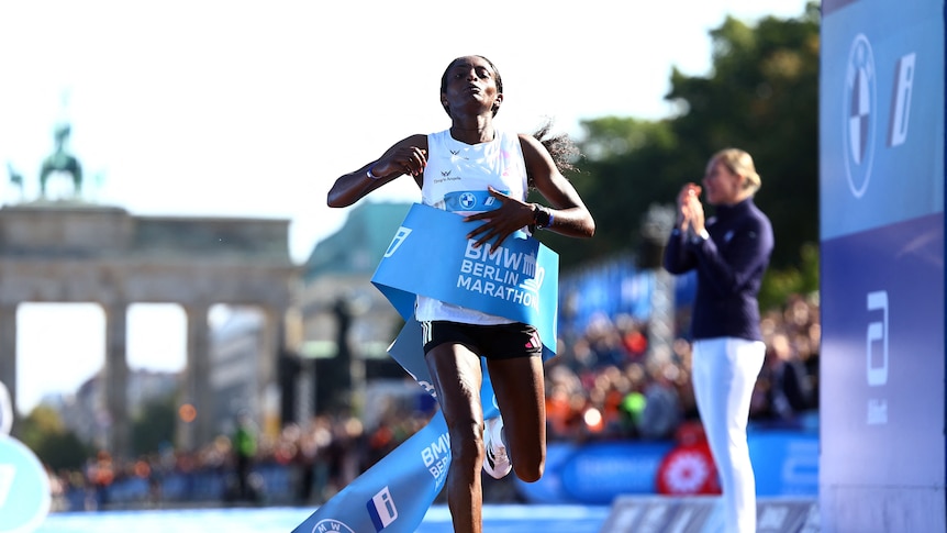 An African female runner breaks the blue finish line ribbon with the Brandenberg Gate behind her