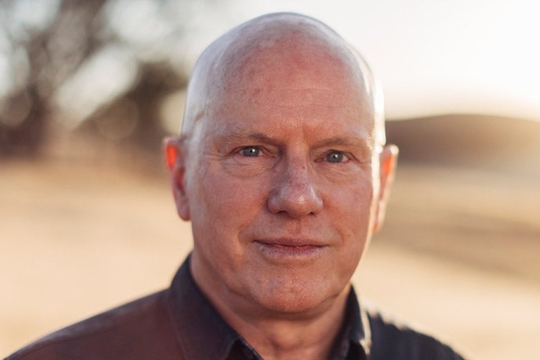 A head shot of balding man, slight smile, background blurred. 