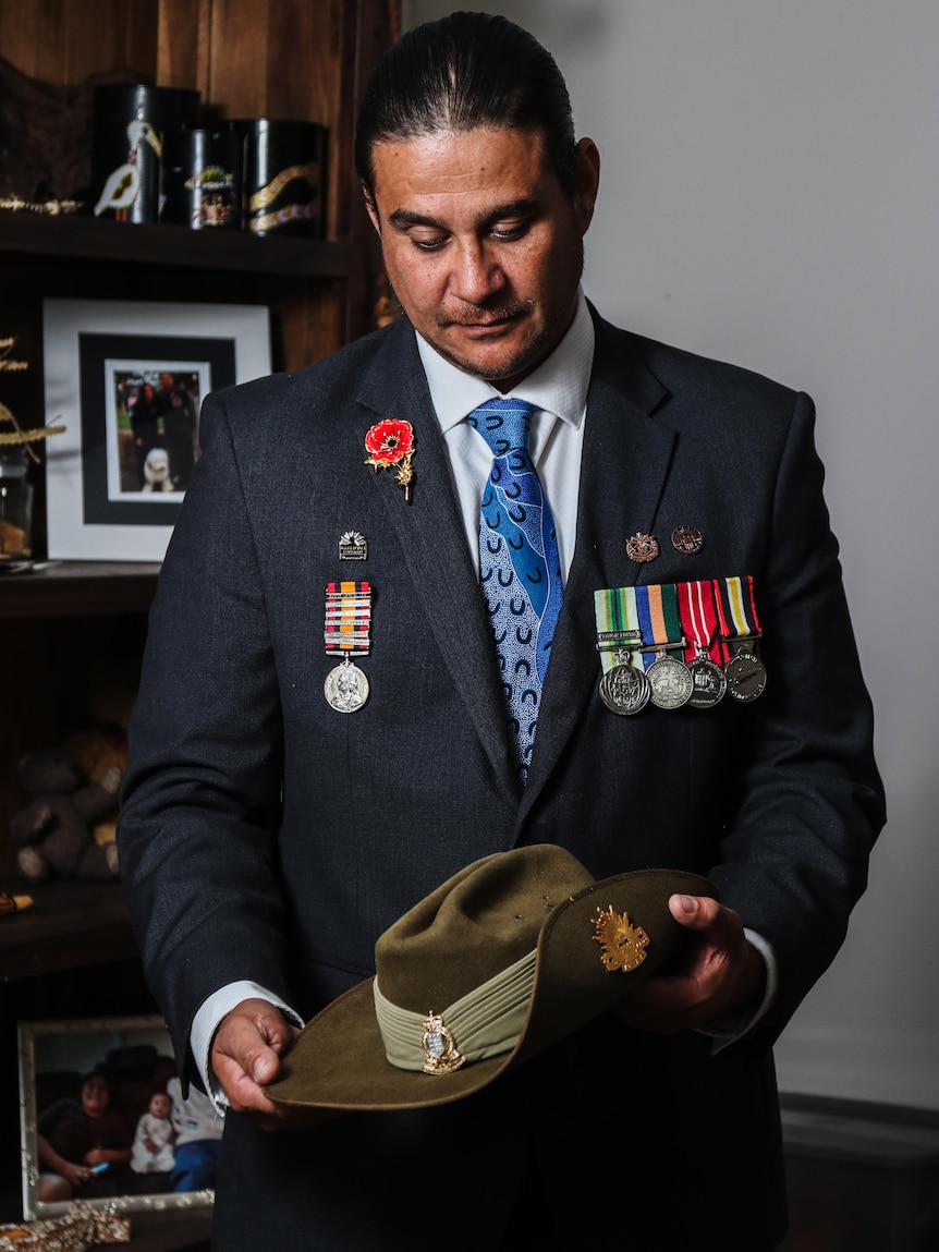 A man with military medals on his suit looks down at the slouched hat in his hands