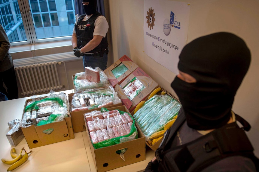 Police and custom officers guard a table showing seized cocaine in crates of imported bananas.