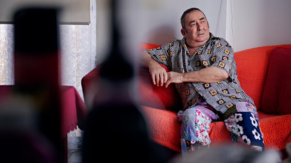 An older man sits on a red couch and looks away