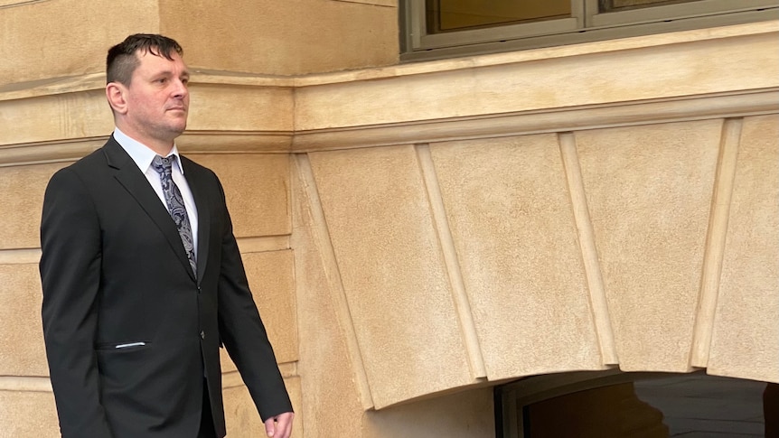A man in a black suit walking beside a court building