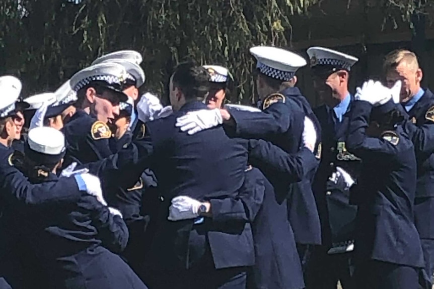 Tasmanian police officers in full uniform hug each other under a tree